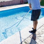 Homme nettoyant la piscine à la maison, debout avec l'appareil de nettoyage